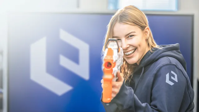 Eine Kollegin von TORUTEC mit einer Nerf-Pistole vor der Logowand
