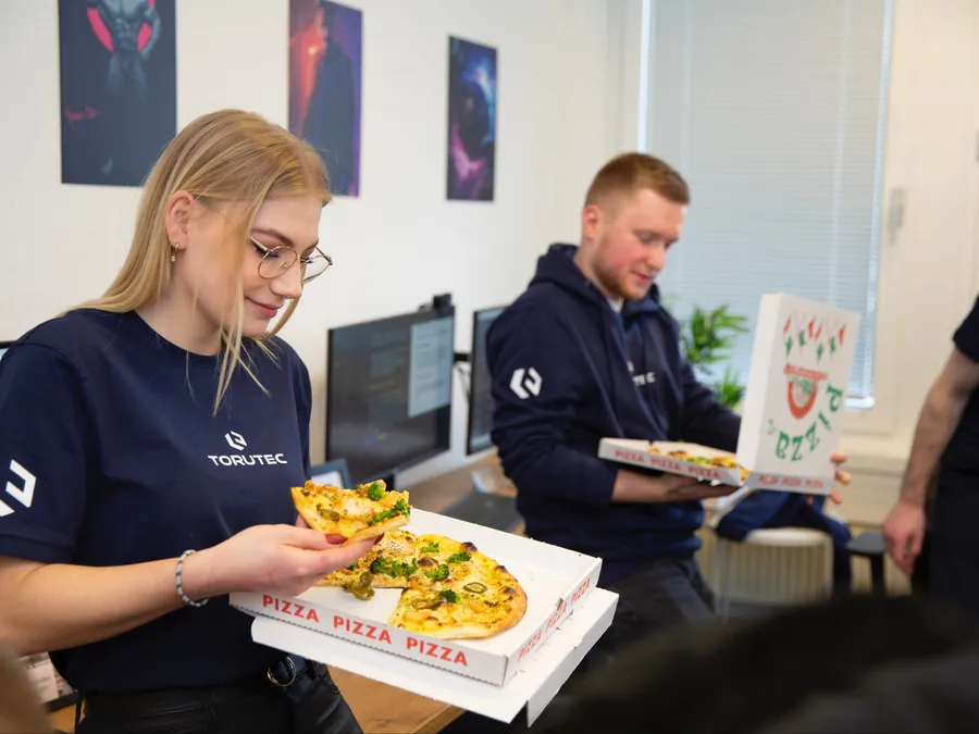 Zwei Kolleginnen und Kollegen mit Pizza am Arbeitsplatz